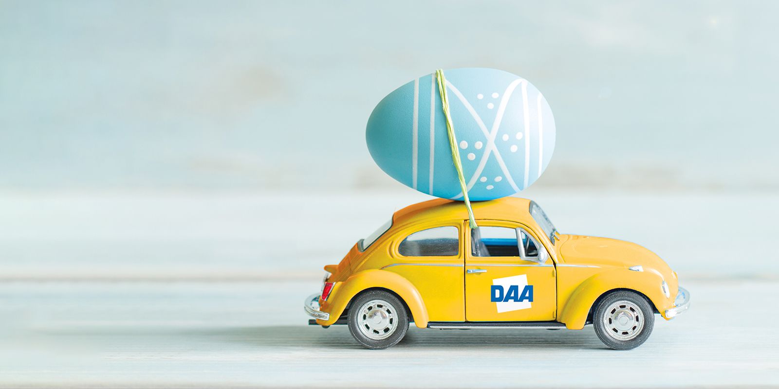 ein dickes Osterei wird auf einem gelben VW-Käfer mit DAA-Logo transportiert