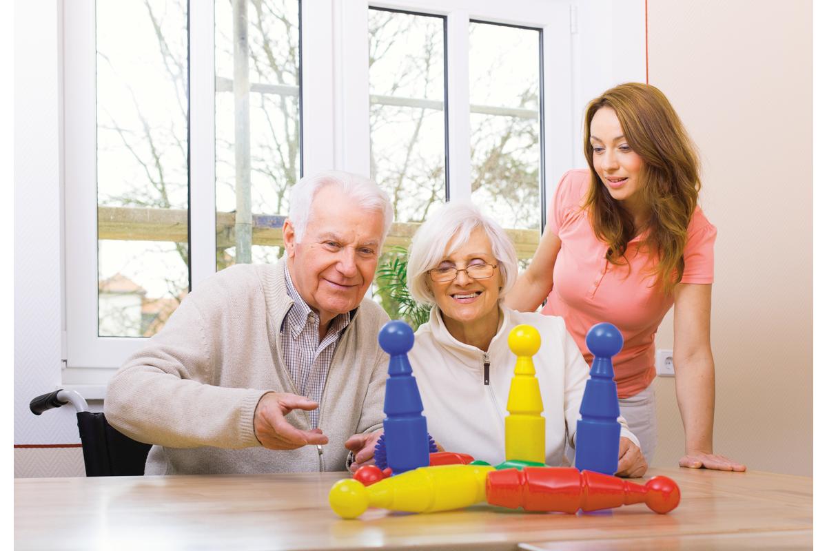 Eine jüngere Frau mit einem älteren Paar spielen gemeinsam ein Kegelspiel