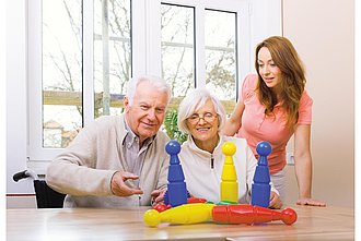 eine Frau spielt mit einem älteren Herrn und einer älteren Dame ein Kegelspiel