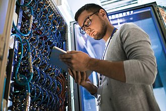 ein junger Mann mit Brille arbeitet in einem Serverraum